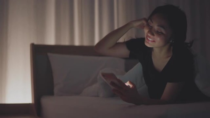 年轻女子在床上用智能手机微笑