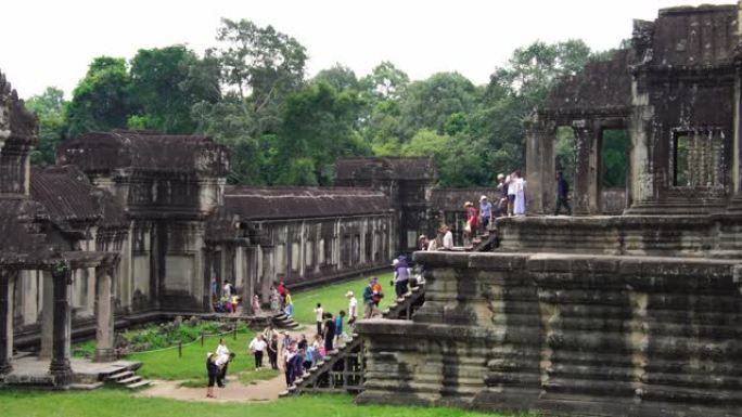 在吴哥窟寺庙废墟中行走的游客。树木生长在建筑物中。联合国教科文组织历史遗址。著名的旅游目的地为背包客