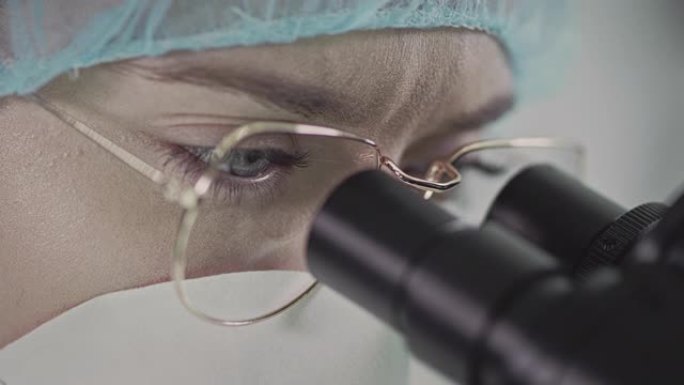 戴着眼镜和医院帽子的女人通过显微镜看