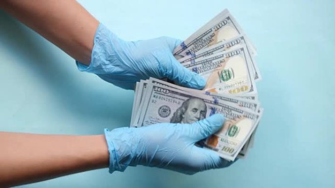戴着医疗手套的手在蓝色背景下数钱。医生数钱。腐败或昂贵医疗保健的概念。
