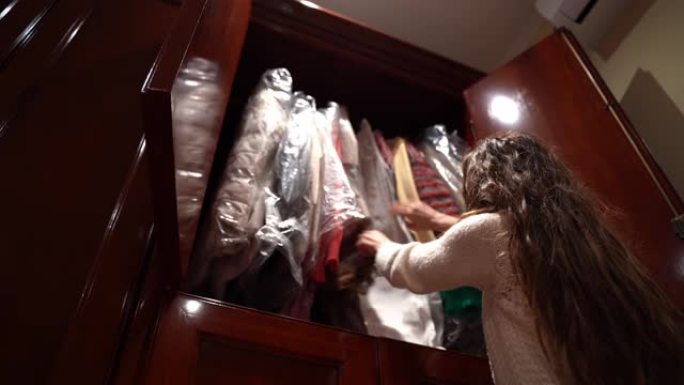 黑发女孩在她的木制衣柜里翻找，女人在衣架上选择衣服，决定穿什么。家里的衣柜，选择问题概念