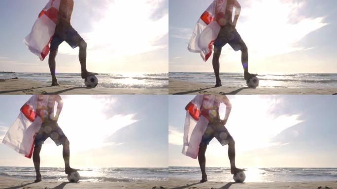 戴着斗篷的年轻人站在海边沙滩上的足球上，看着日落时海滩上的海洋摄像机steadycam万向节旋转
