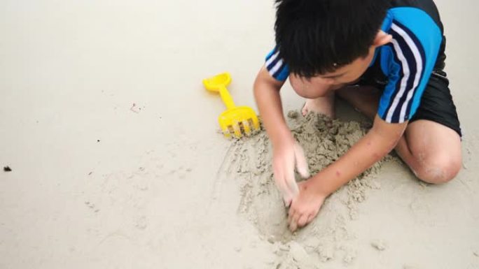暑假亚洲家庭旅游休闲出海男孩玩沙子与活跃在海滩上，独自在下午建造了一座沙堡