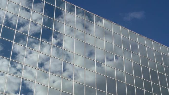 在晴天，漂浮在蓝天上的云彩映照在一座高高的玻璃建筑的窗户上。概念。4K