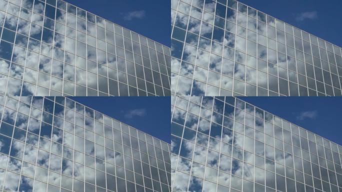 在晴天，漂浮在蓝天上的云彩映照在一座高高的玻璃建筑的窗户上。概念。4K
