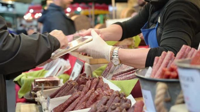一名男子用手指在平板电脑上签名，以支付在伦敦Borough Market的一个摊位上购买熟肉的费用。