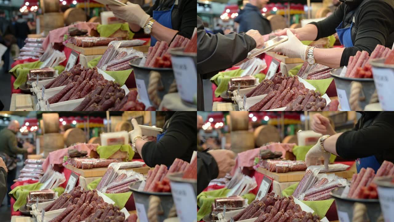 一名男子用手指在平板电脑上签名，以支付在伦敦Borough Market的一个摊位上购买熟肉的费用。