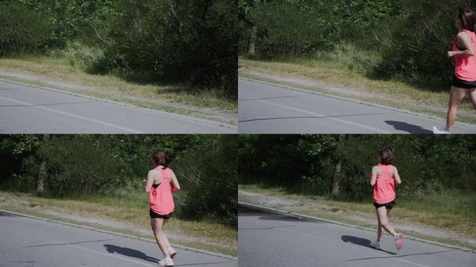 公园里跑步的年轻运动女性。穿着粉色运动服和耳机的迷人女孩在公园练习。在森林里训练女跑步者。有脂肪团的