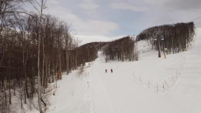 滑雪者和滑雪者乘坐滑雪缆车，而人们则在冬季滑雪胜地的背景中滑雪。