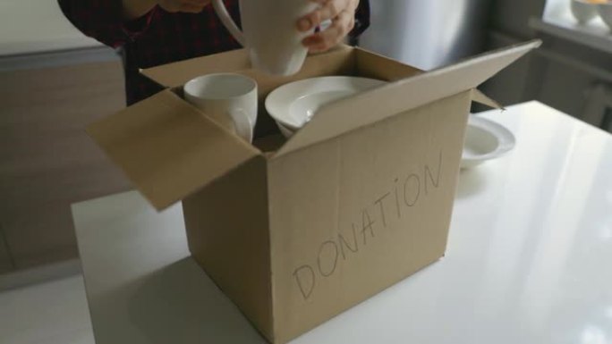 捐赠家居用品-妇女将餐具放在纸板箱中捐赠在厨房桌子上
