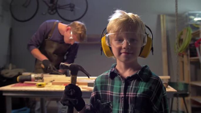 戴眼镜的男孩用锤子站着，看着相机