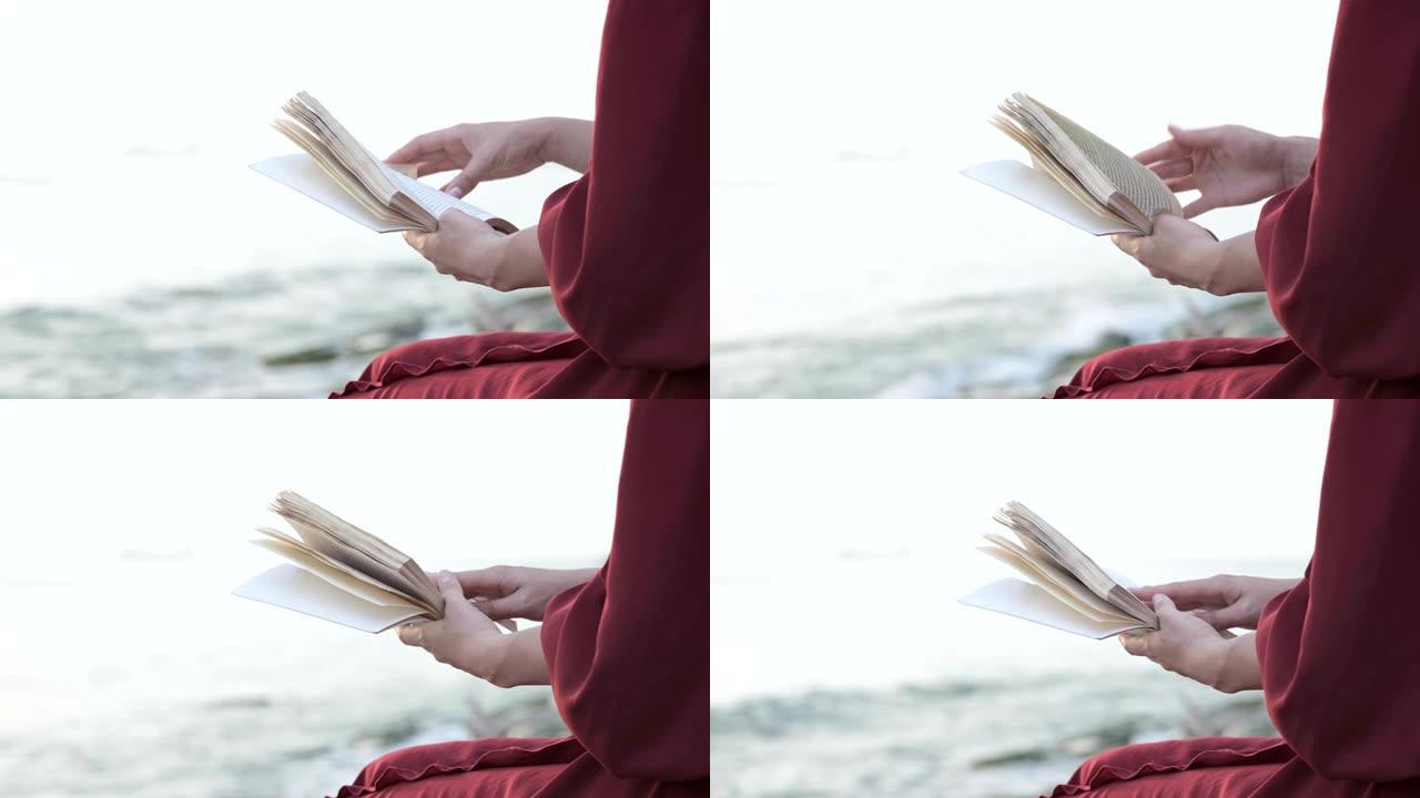 坐在海边时，穿着红色连衣裙的女孩从后面看到的景色读到了一本书。双手特写