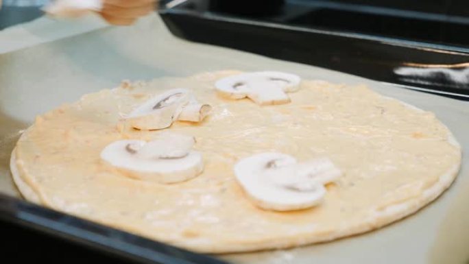 双手将蘑菇添加到比萨饼面团中。女人在厨房准备披萨，特写。厨师在披萨中添加食材