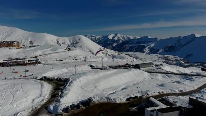 冬季滑翔伞运动。降落伞的天空潜水员在阳光明媚的冬日飞越滑雪胜地。俯视图。高加索山脉，格鲁吉亚，古达乌