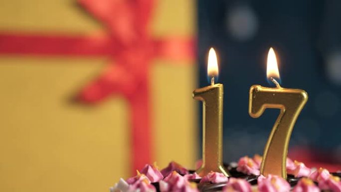 生日蛋糕编号17点灯燃烧的金色蜡烛，蓝色背景礼物黄色盒子用红丝带绑起来。特写和慢动作