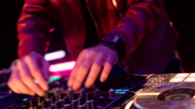 夜总会迪斯科派对中Dj调音台控制器的特写。DJ手触摸按钮和滑块播放电子音乐。DJ手在乙烯基板上混合和