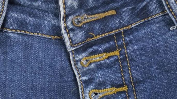 旋转，特写，蓝色牛仔牛仔裤的细节，前视图皮带环，口袋和纽扣孔。时尚背景。