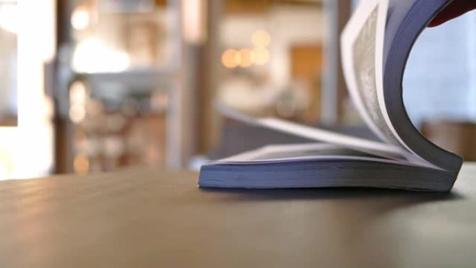 双手翻转放在咖啡馆木桌上的书页。