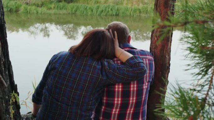 一对相爱的夫妇在松树林地的河岸上拥抱。在森林海岸拥抱男人的女人。浪漫的情侣在夏日森林的河边享受大自然