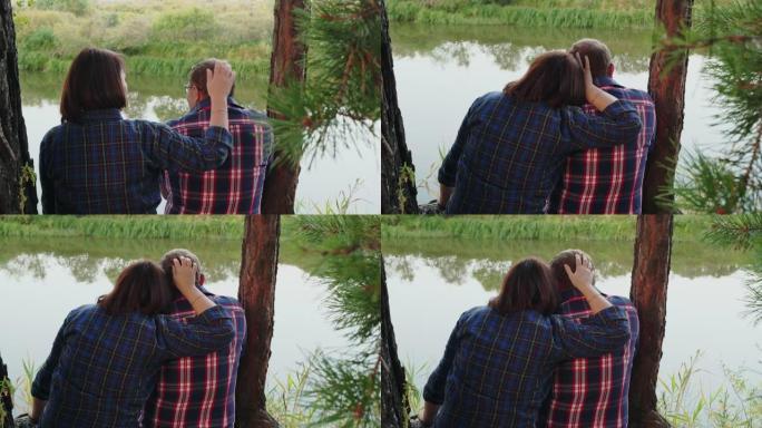 一对相爱的夫妇在松树林地的河岸上拥抱。在森林海岸拥抱男人的女人。浪漫的情侣在夏日森林的河边享受大自然