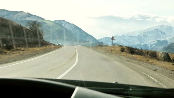 从汽车的挡风玻璃上看，在美丽的山脉和云的背景下，沿着山路柏油路行驶的汽车