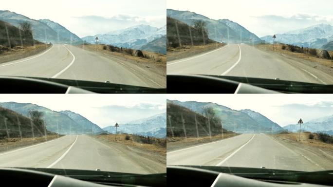 从汽车的挡风玻璃上看，在美丽的山脉和云的背景下，沿着山路柏油路行驶的汽车