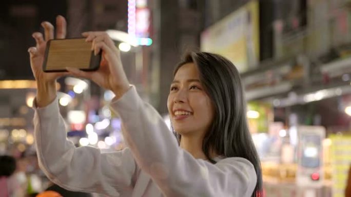 快乐年轻的亚洲女性在夜市使用智能手机