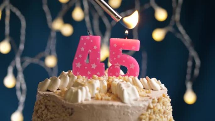 蓝色背景上有45号粉色蜡烛的生日蛋糕。蜡烛着火了。慢动作和特写视图