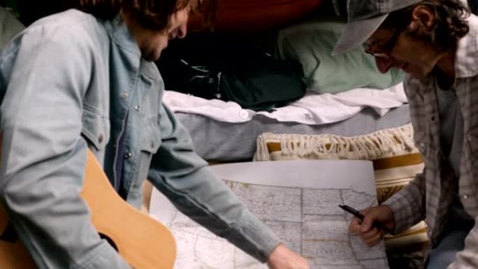 两名男子计划在美国的公路旅行，看着并指向一张纸质地图