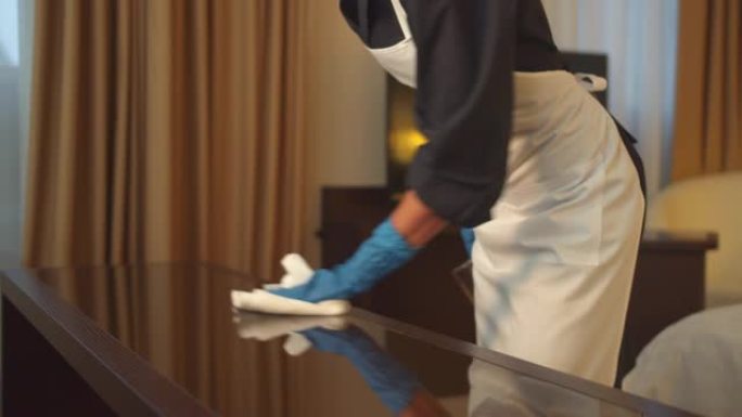 戴着手套的女佣在酒店房间用抹布擦拭桌子