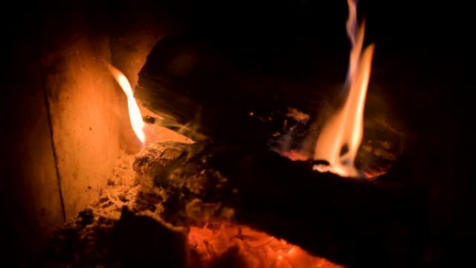 夜间在耐火玻璃后面的现代家用炉灶中，用煤昏暗燃烧的柴火的特写镜头。低调。摄像机转动时靠近火炉移动。环