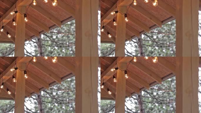 雨滴从装饰有灯泡的木制屋顶流出。/森林中的夏季雨天。