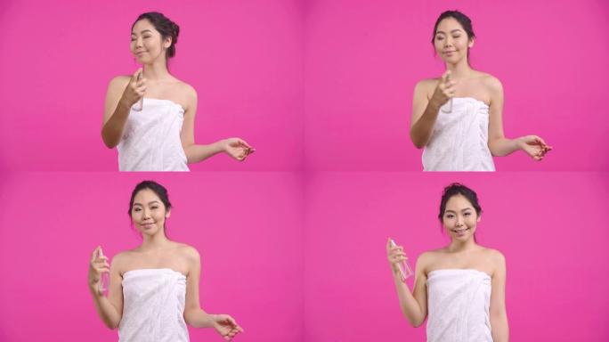 快乐的亚洲女孩应用面部喷雾孤立在粉红色