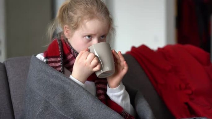 一个生病的孩子的肖像，戴着围巾和格子，在公寓的沙发上喝杯热茶