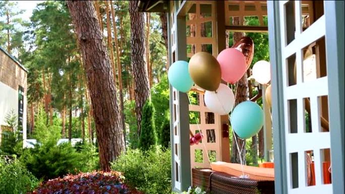 一堆不同的彩色氦气球在风中玩耍，绑在木制的户外凉亭露台上，作为儿童活动日派对的装饰。