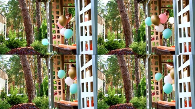 一堆不同的彩色氦气球在风中玩耍，绑在木制的户外凉亭露台上，作为儿童活动日派对的装饰。