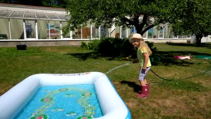 金发女孩在乡村别墅用水管填充充气游泳池。万向节运动