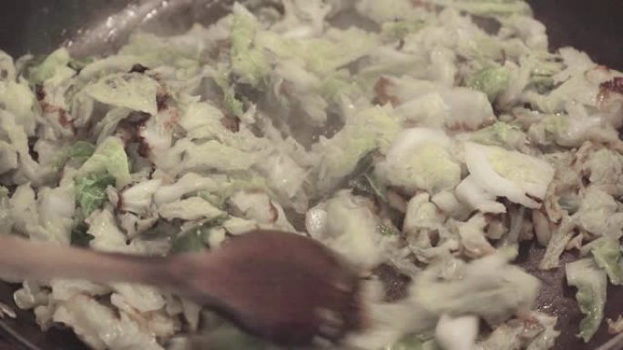 卷心菜蔬菜在平底锅中煎炸，男人的手用木勺搅拌，然后盖上老式颜色等级的蒸玻璃盖