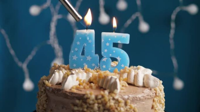 蓝色背景上有45号蜡烛的生日蛋糕。蜡烛着火了。慢动作和特写视图