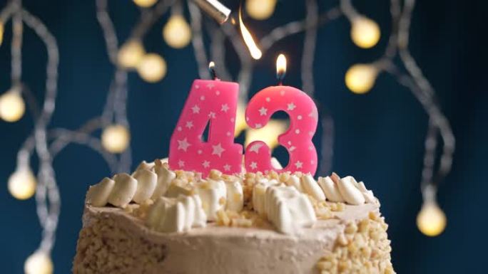 蓝色背景上有43号粉色蜡烛的生日蛋糕。蜡烛着火了。慢动作和特写视图