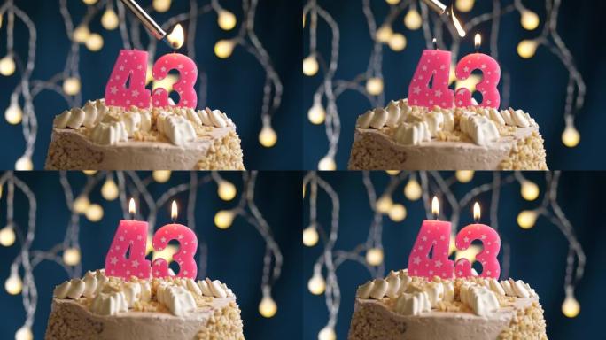 蓝色背景上有43号粉色蜡烛的生日蛋糕。蜡烛着火了。慢动作和特写视图