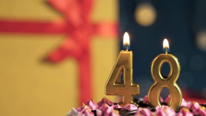 生日蛋糕编号48点灯燃烧的金色蜡烛，蓝色背景礼物黄色盒子用红丝带绑起来。特写和慢动作