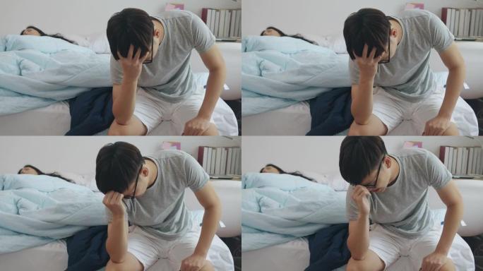 压力男人坐在床上，而他的女朋友睡觉。