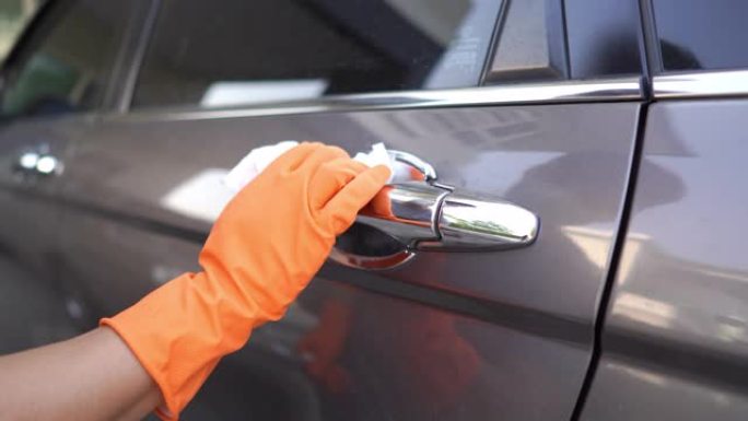 手在家里的车库里用手套擦拭灰色汽车清洁新型冠状病毒肺炎病毒的门把手表面。