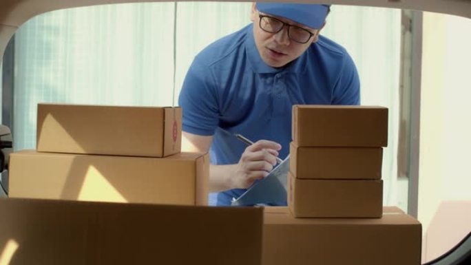 亚洲送货员在送货车后部检查和携带纸质包裹箱。邮政递送服务的概念。4k UHD中的慢动作。