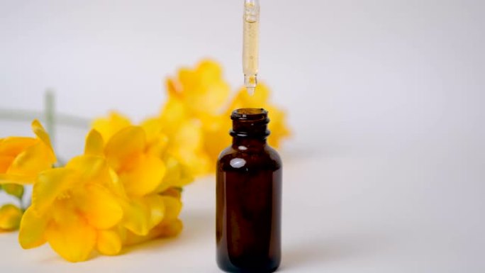 精油从化妆品移液器滴落到模糊的黄色花朵上的容器中。