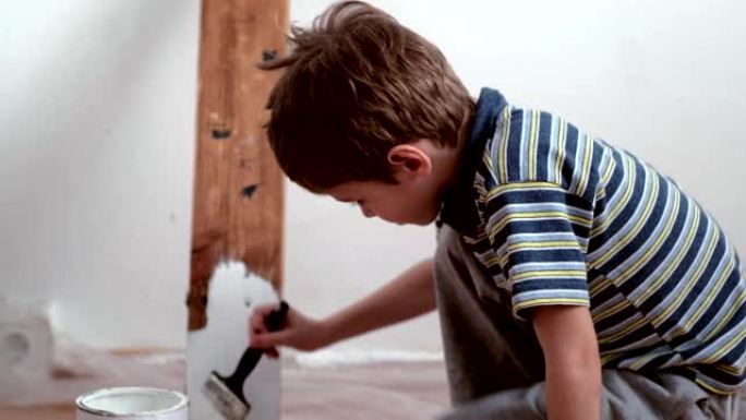 一个5岁的男孩用白色油漆在架子上涂漆。白色背景。