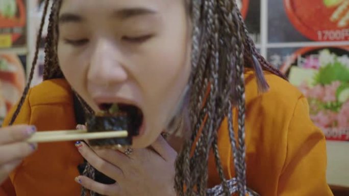 亚洲年轻女子在亚洲餐厅用筷子吃日本寿司卷