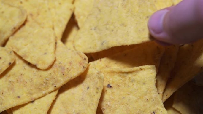 手拿一个玉米片，一个宏观静态镜头。不健康和肥腻的垃圾食品的概念-黄色三角形薯条的山特写4k
