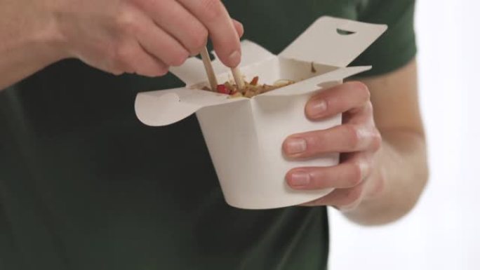 年轻人用白纸盒的筷子吃中国面条和蔬菜。孤立，在白色背景上